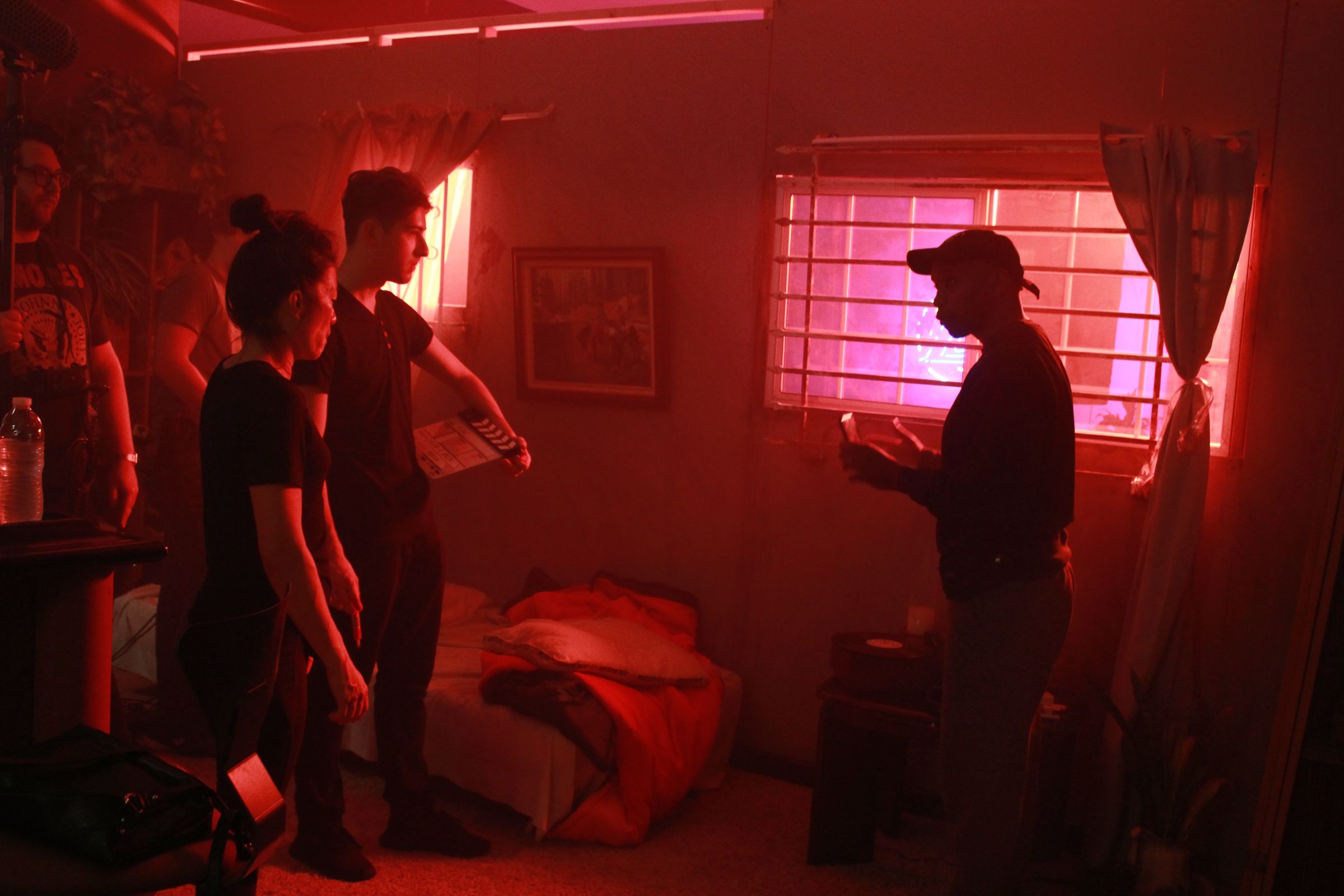 Isaiah Smith reading the scene in the red-lit bedroom set of Bow, with cast and crew