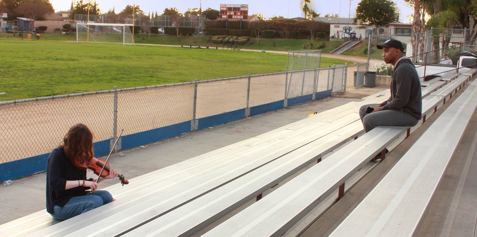 The lead actor plays violin in empty bleachers while Isaiah watches from above, on the set of Bow