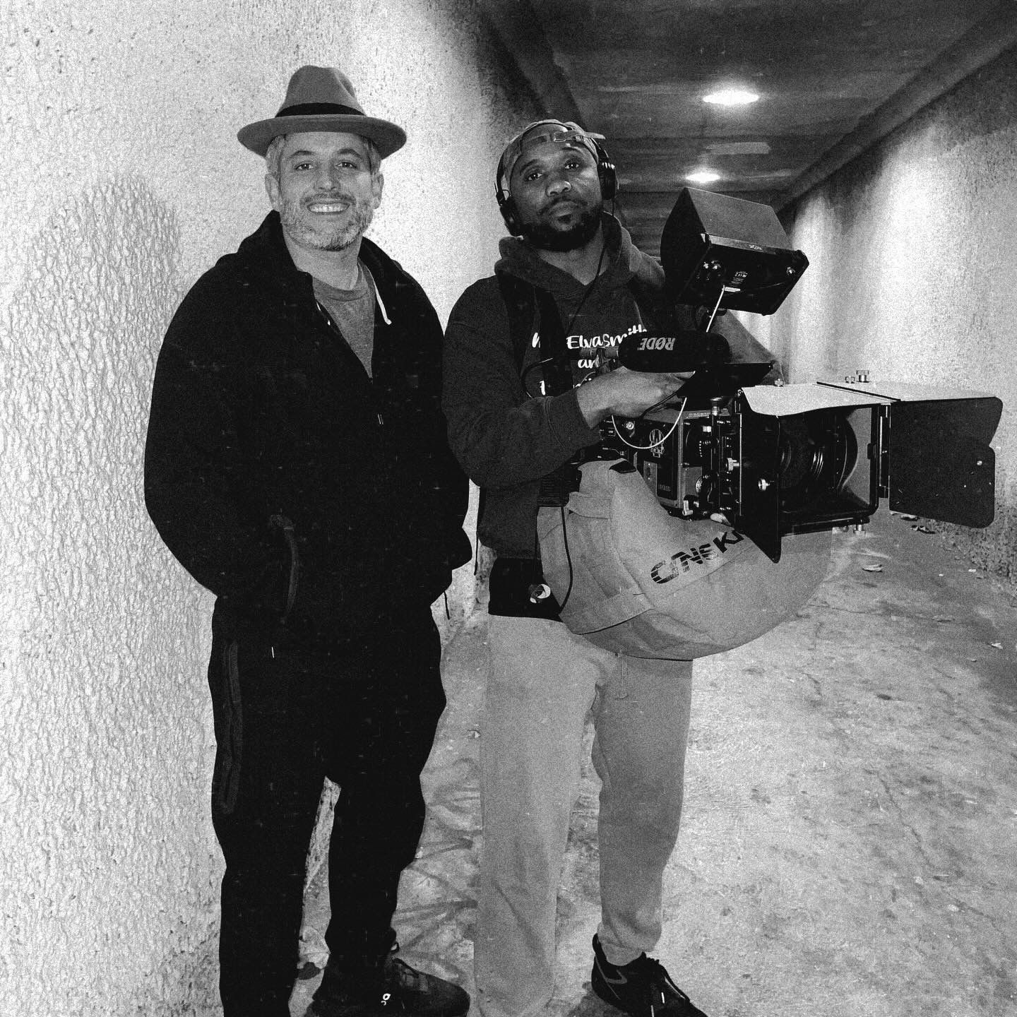 Isaiah with a cinema camera rig beside a friend in a tunnel, black and white