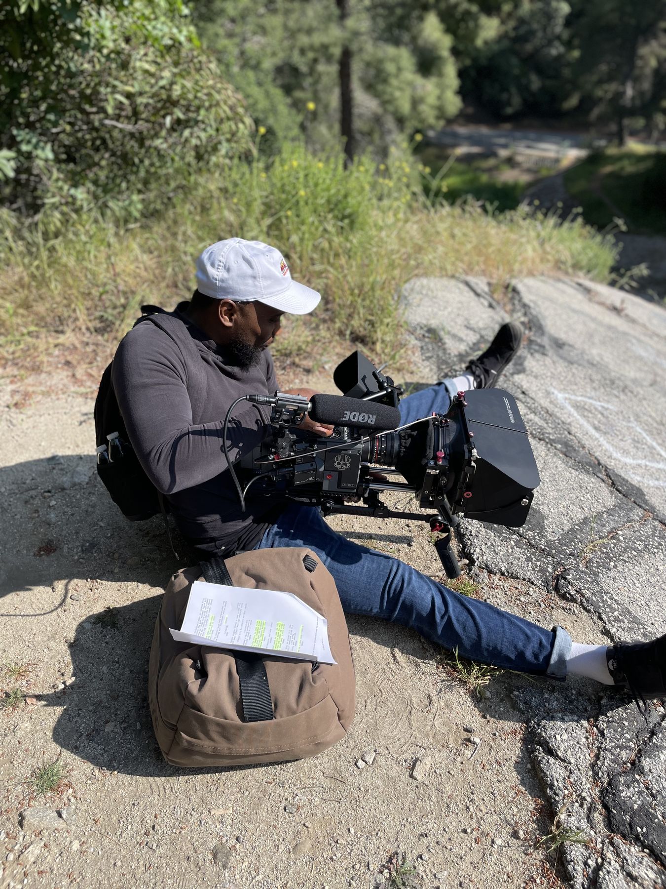 Isaiah sitting on a rock with a cinema camera, script pages on his bag